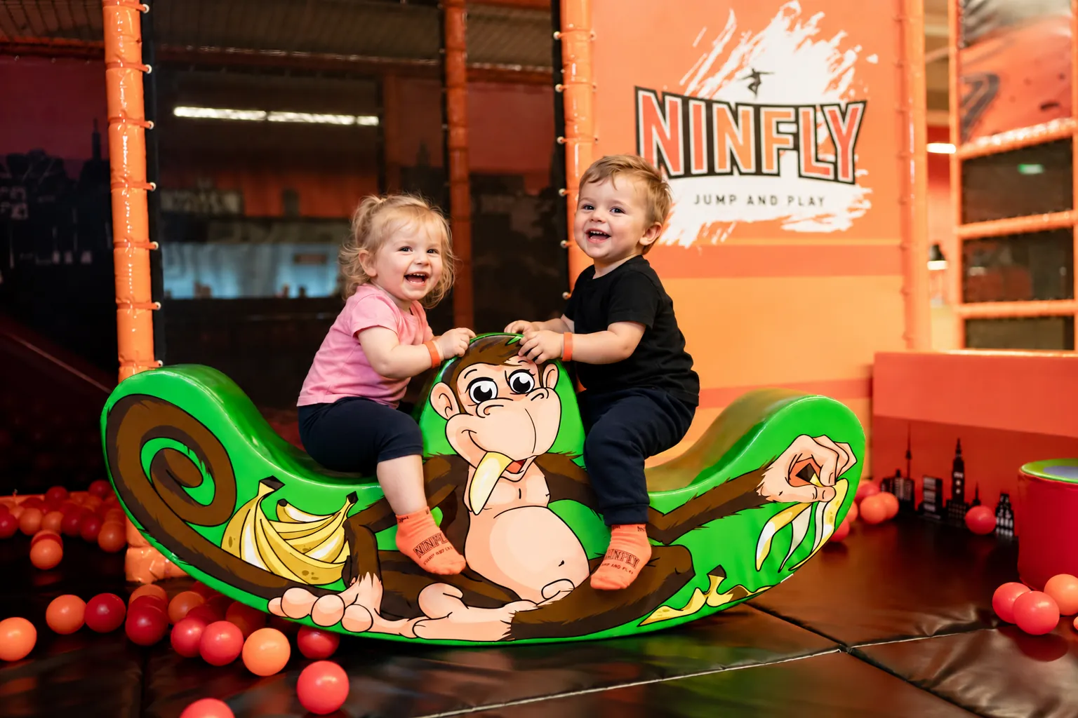 Zwei Kleinkinder sitzen lachend auf der grünen Affen-Wippe im NINFLY